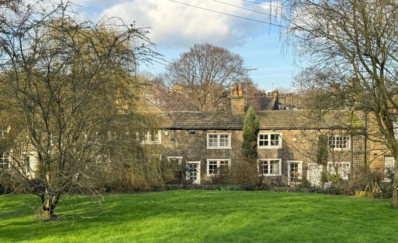 Stone terraced cottages behind a village green in West Yorkshire